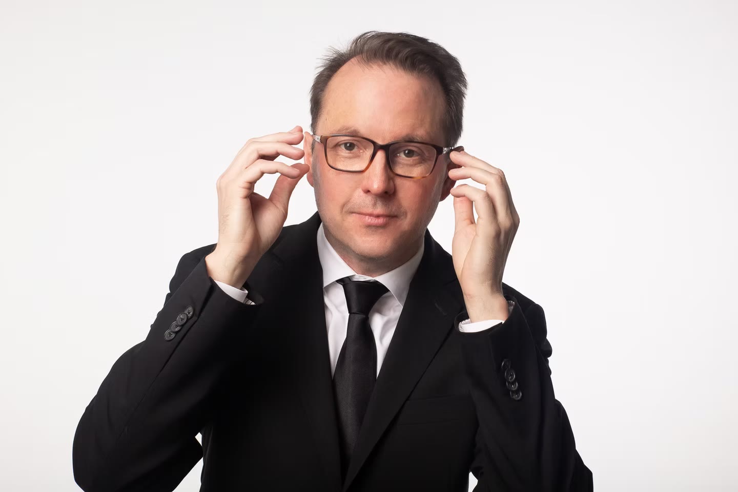 Actor headshot, hands to glasses, black suit on white