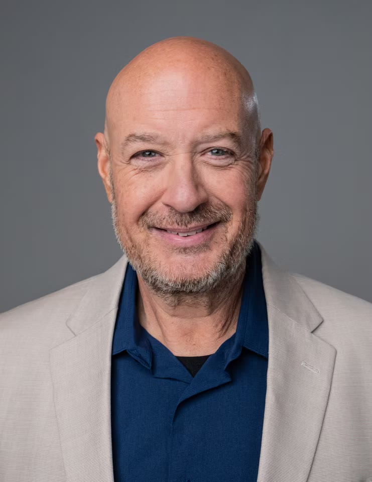 Warm smiling headshot in stone blazer over blue